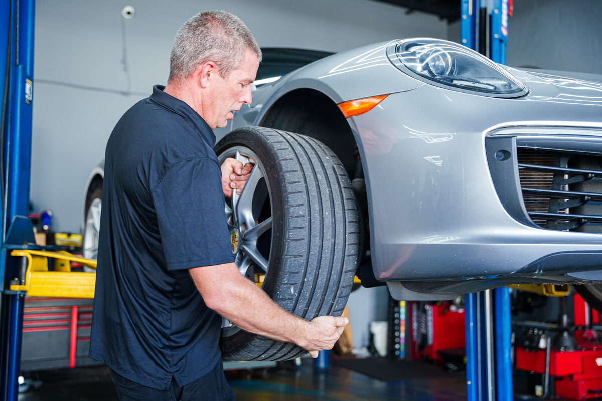 Autobahn technician carrying a wheel and tire beside a Porsche on a lift