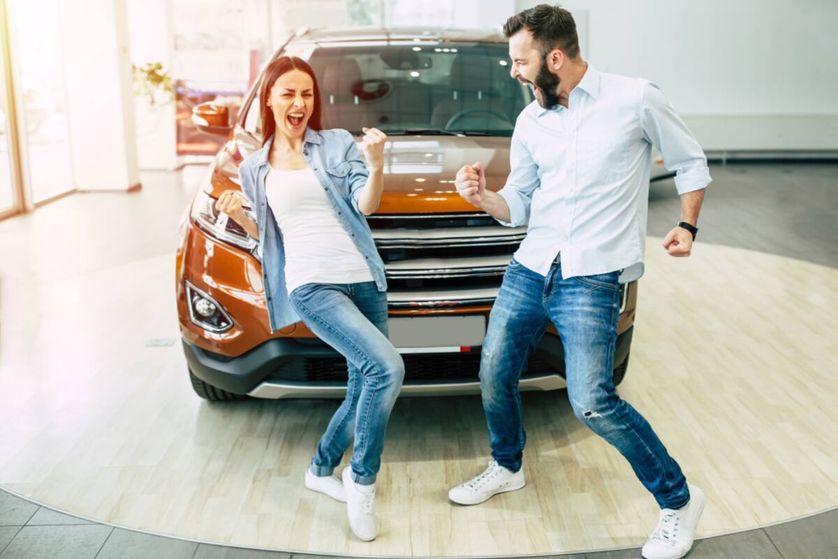 Couple celebrating beside a new car in a showroom