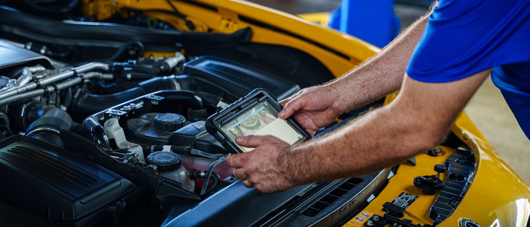 An Autobahn technician holding a tablet over the engine of a Mercedes-AMG