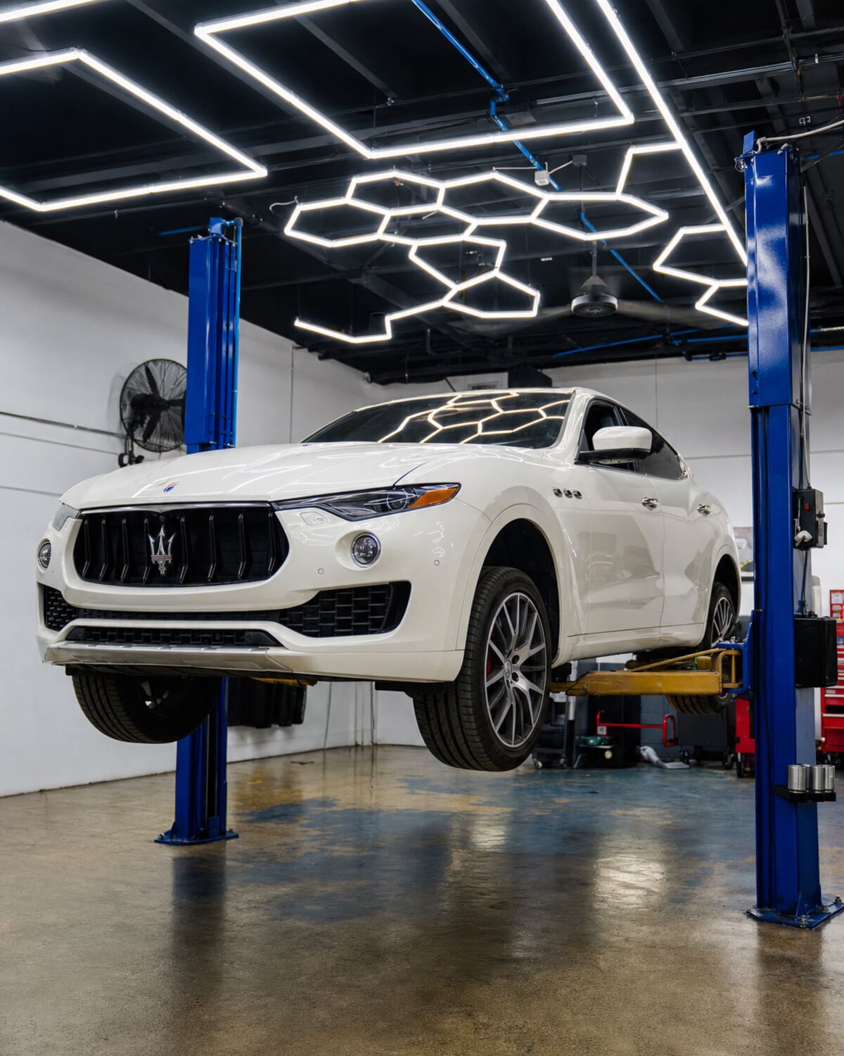 A white Maserati Levante raised on a two-post lift