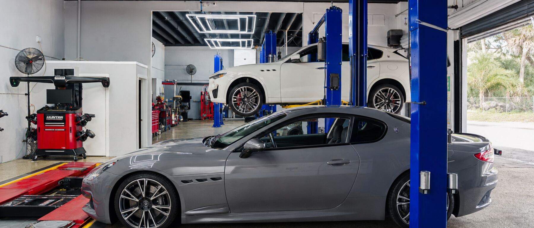 A gray Maserati GranTurismo in a service bay with a Levante on a lift behind it