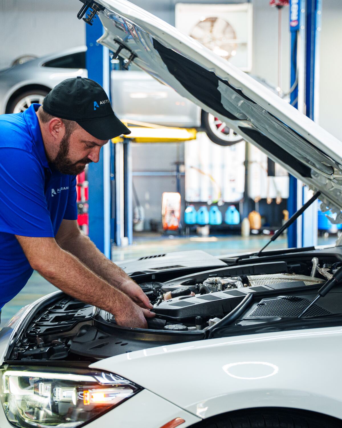 An Autobahn technician working under the hood of a white Mercedes-Benz